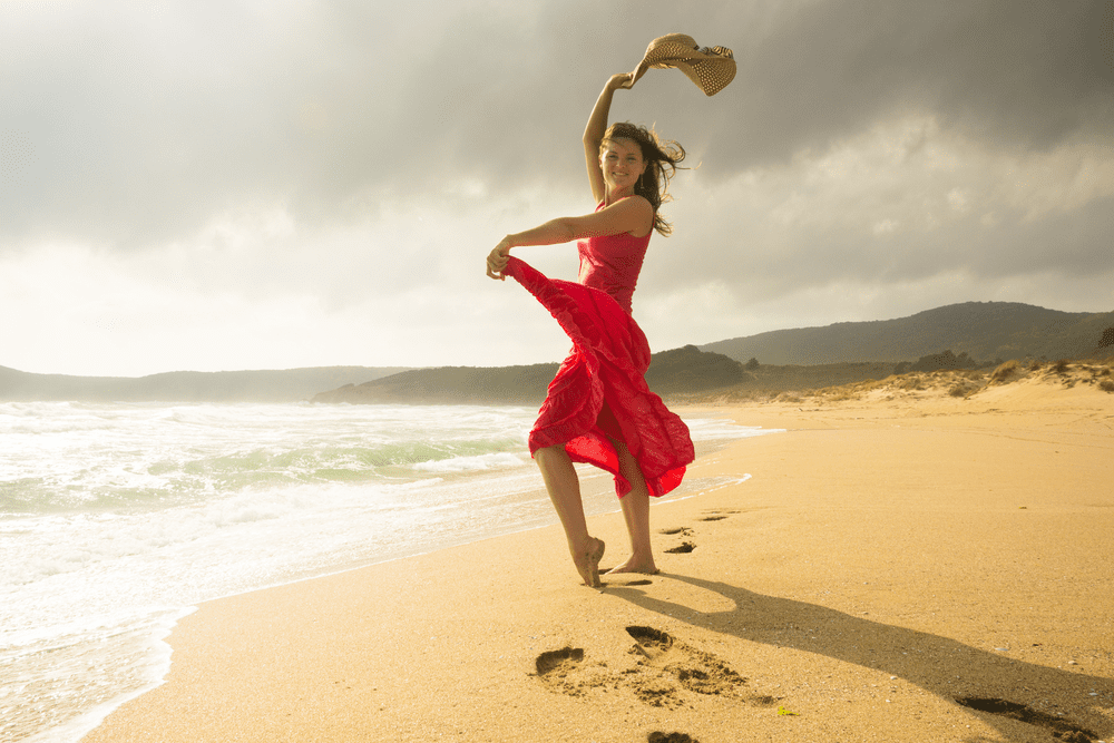 A woman in a red dress is elegantly dancing on the beach, showcasing her mesmerizing body lift.